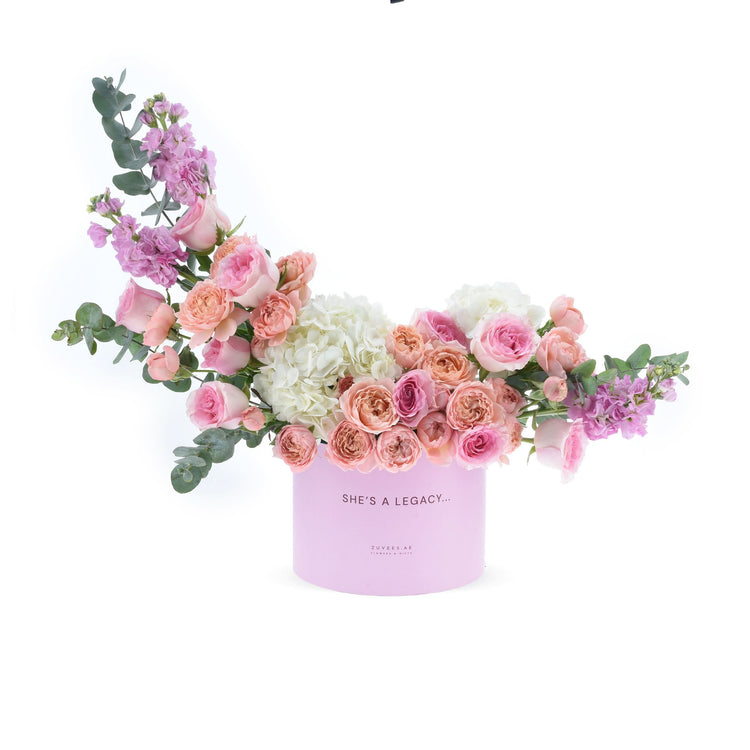 Soft pink roses, hydrangeas, and eucalyptus in a lavender box reading "She&