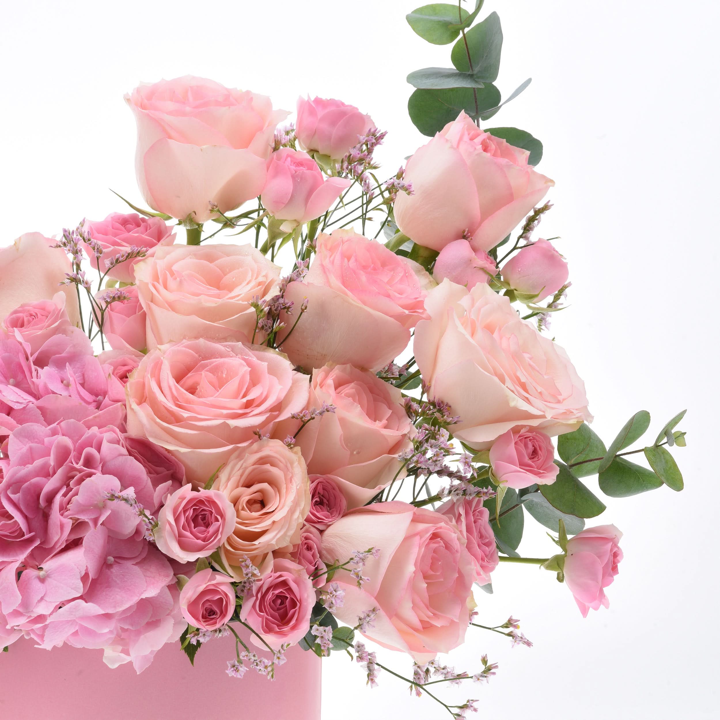 Soft pink roses, hydrangeas, and eucalyptus in a pastel pink vase.