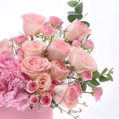 Soft pink roses, hydrangeas, and eucalyptus in a pastel pink vase.