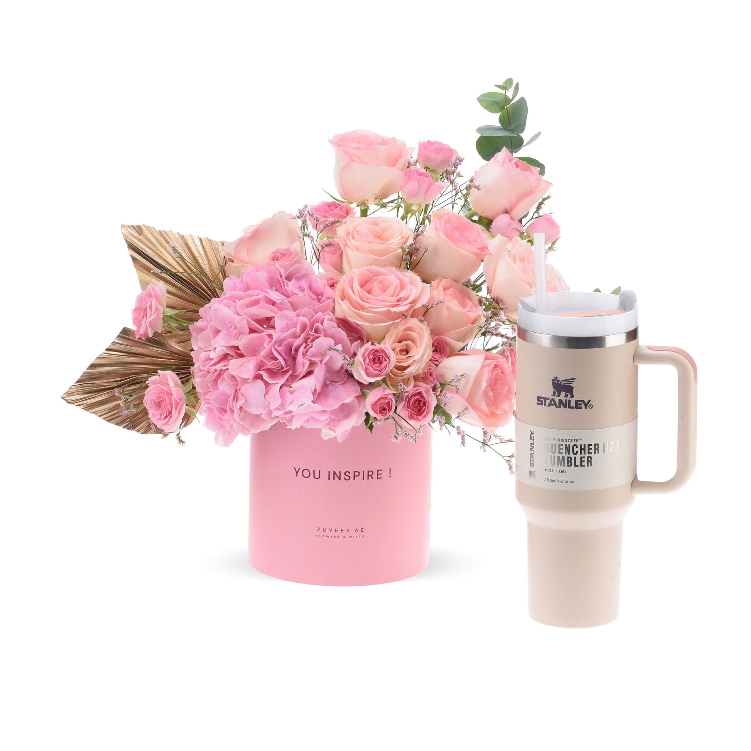 Pink roses and hydrangeas in branded vase beside beige Stanley tumbler.