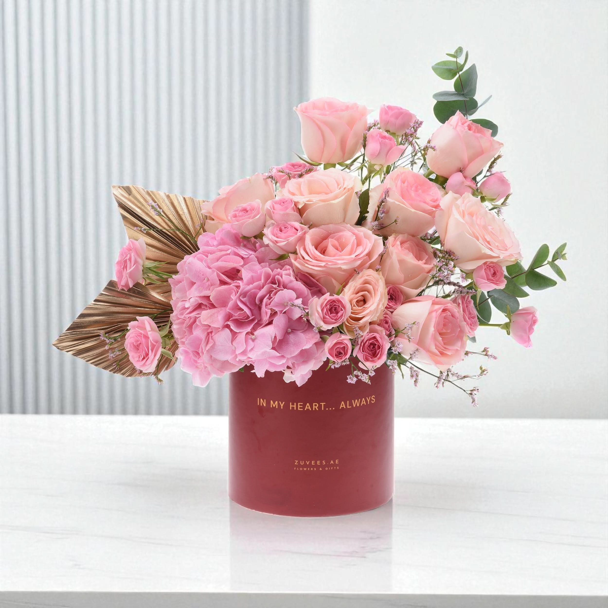Soft pink roses and hydrangeas bloom in a matte red vase with gold text.