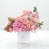 Pink roses, hydrangeas, gold palm leaves in white Zuvees box on marble.