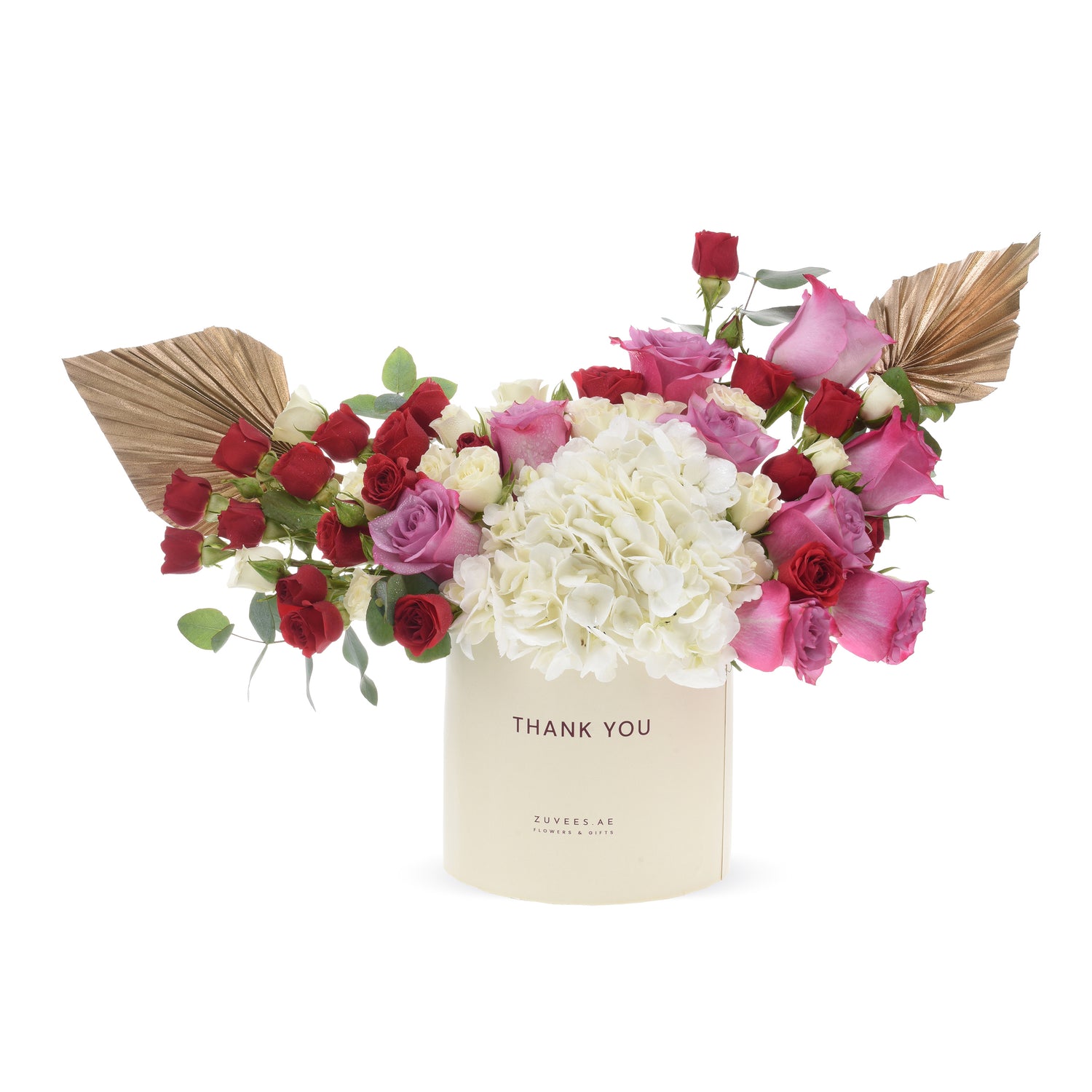 Cream box holds vibrant red, pink, white roses and hydrangeas, accented with gold fan leaves.