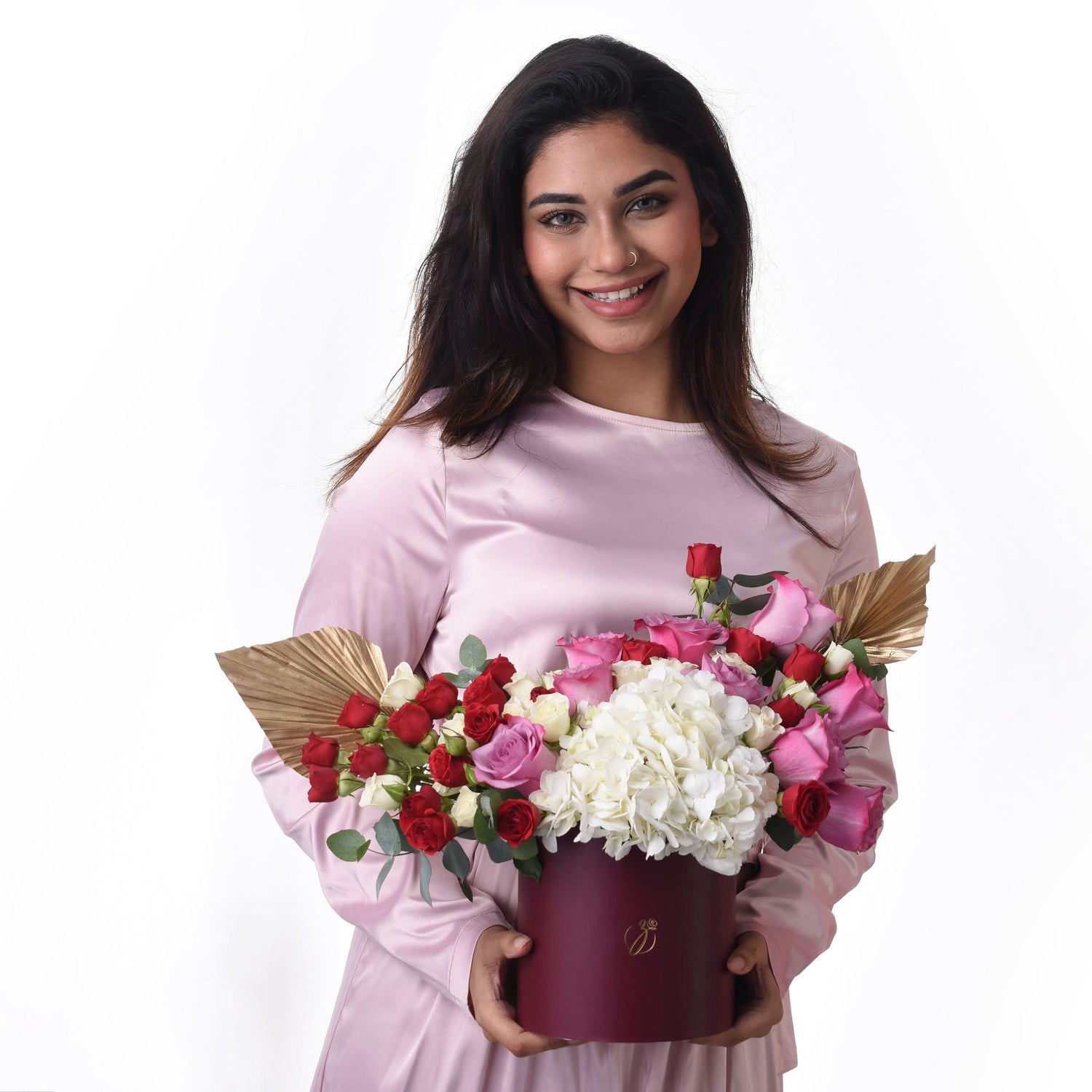 Woman holds burgundy box with red, pink roses and white hydrangeas, gold accents.