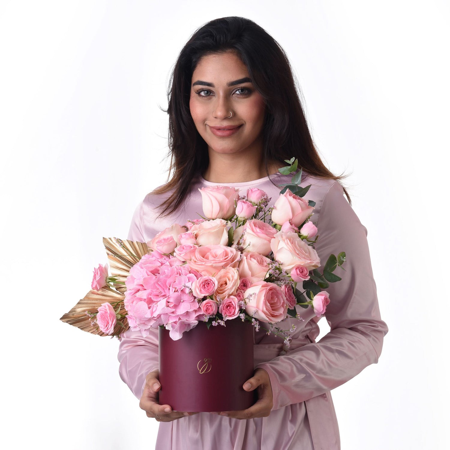 Pink roses and hydrangeas in burgundy box, held by smiling woman.