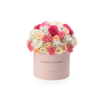 Pink box with "CONGRATULATIONS," holding vibrant pink, peach, white roses and carnations.