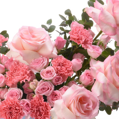 Soft pink roses and carnations with lush greenery against white background.