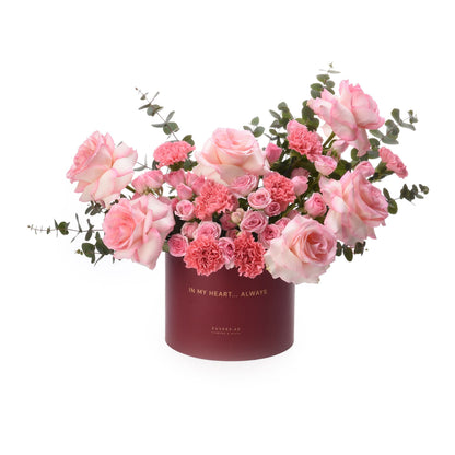 Soft pink roses and carnations in elegant burgundy box with gold text.