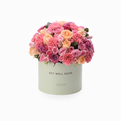 Pastel pink roses and carnations bloom in mint-green "Get Well Soon" box.