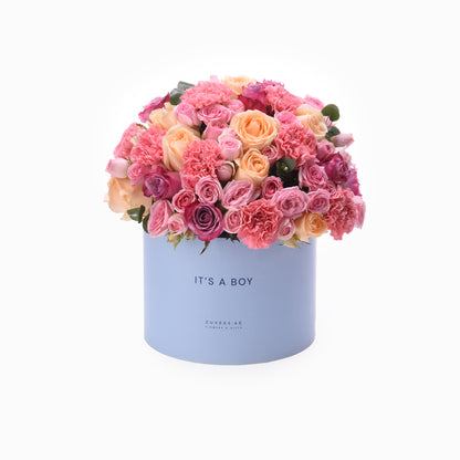 Pastel pink roses and carnations overflow a light blue “It’s a Boy” gift box.