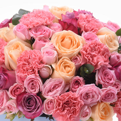 Vibrant pink and peach roses blend with ruffled carnations, dewdrops glisten.