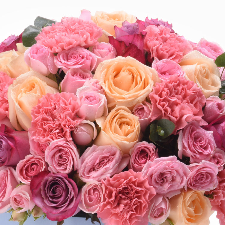 Vibrant pink and peach roses blend with ruffled carnations, dewdrops glisten.