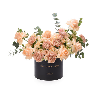 Soft peach roses and carnations in sleek black box with gold "Happy Anniversary" text.