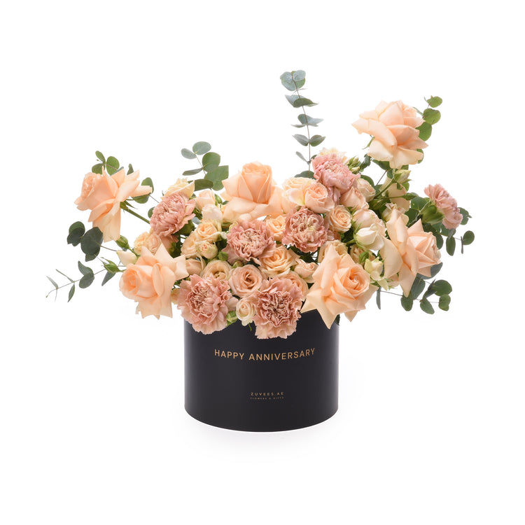 Soft peach roses and carnations in sleek black box with gold "Happy Anniversary" text.